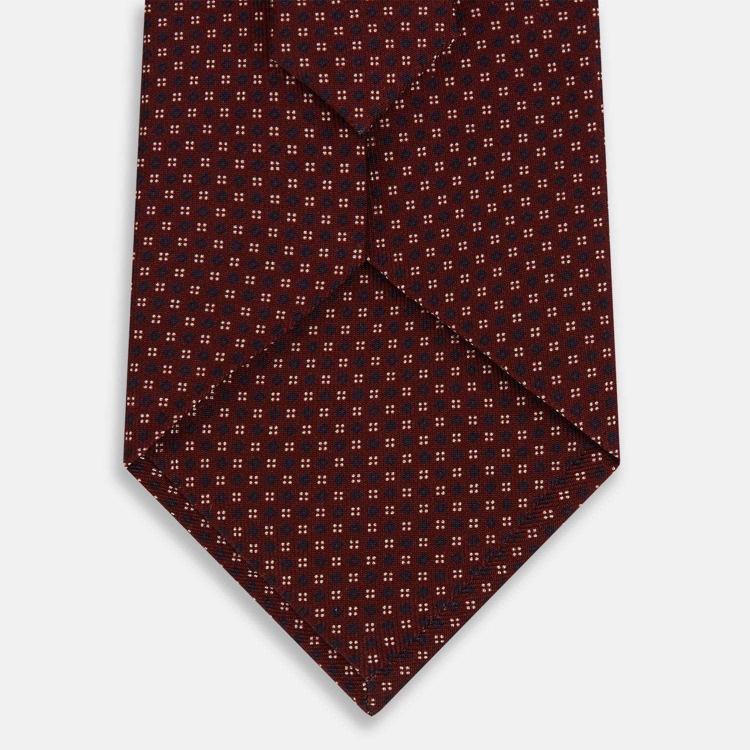 View 3 of product The Burgundy Geometric Motif Silk Tie by Turnbull & Asser features blue and white dots and is displayed neatly rolled on a plain white background.