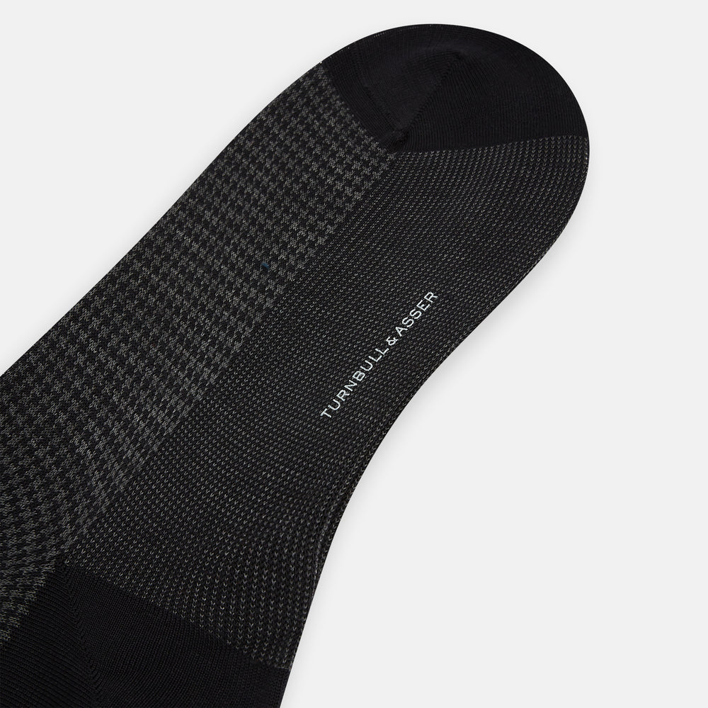 The Turnbull & Asser Charcoal Melange Houndstooth Long Sock is knee-high, with a subtle dark houndstooth pattern and solid black toe, heel, and cuff, shown on a white background.