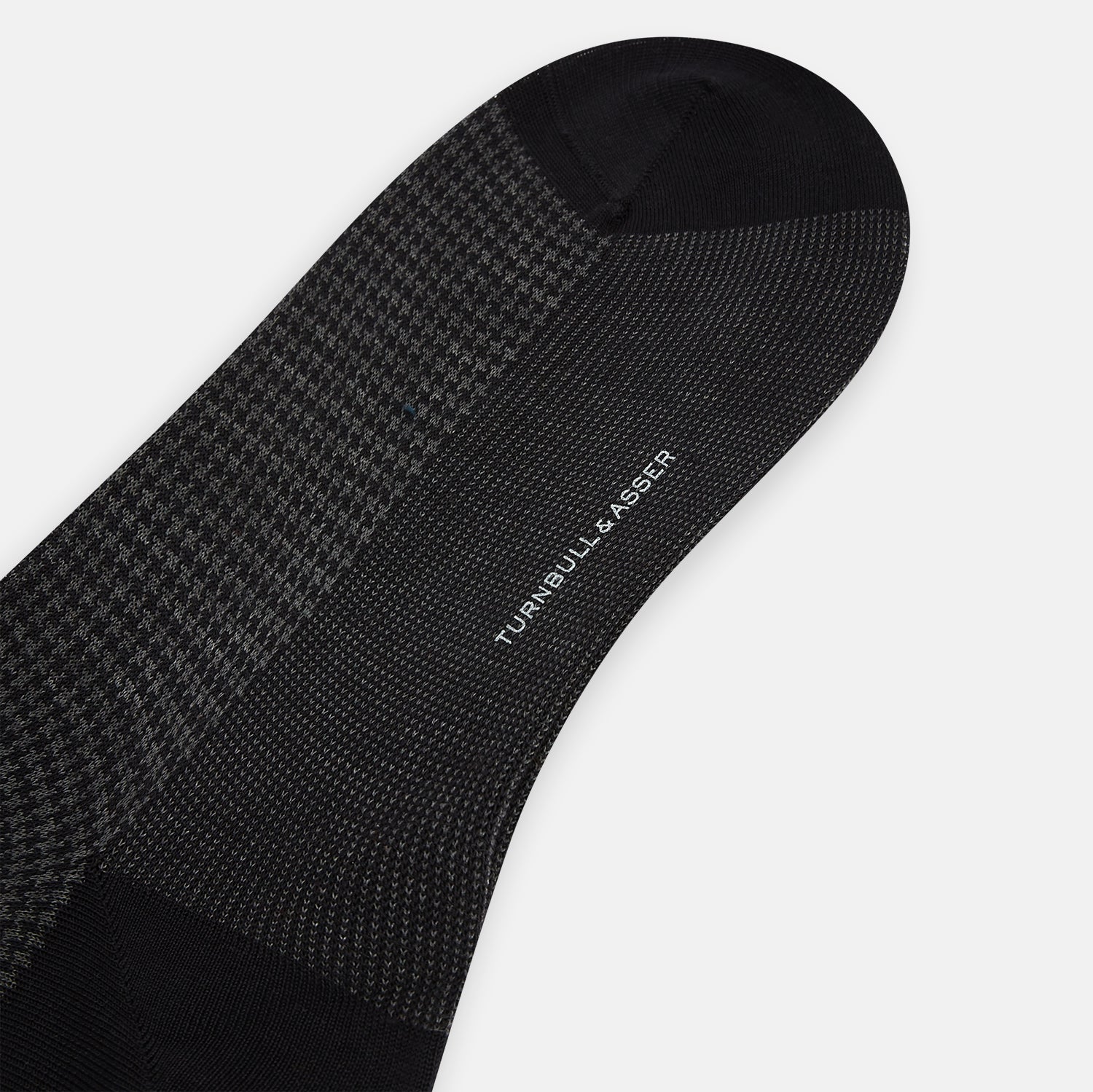 View 3 of product The Turnbull & Asser Charcoal Melange Houndstooth Long Sock is knee-high, with a subtle dark houndstooth pattern and solid black toe, heel, and cuff, shown on a white background.