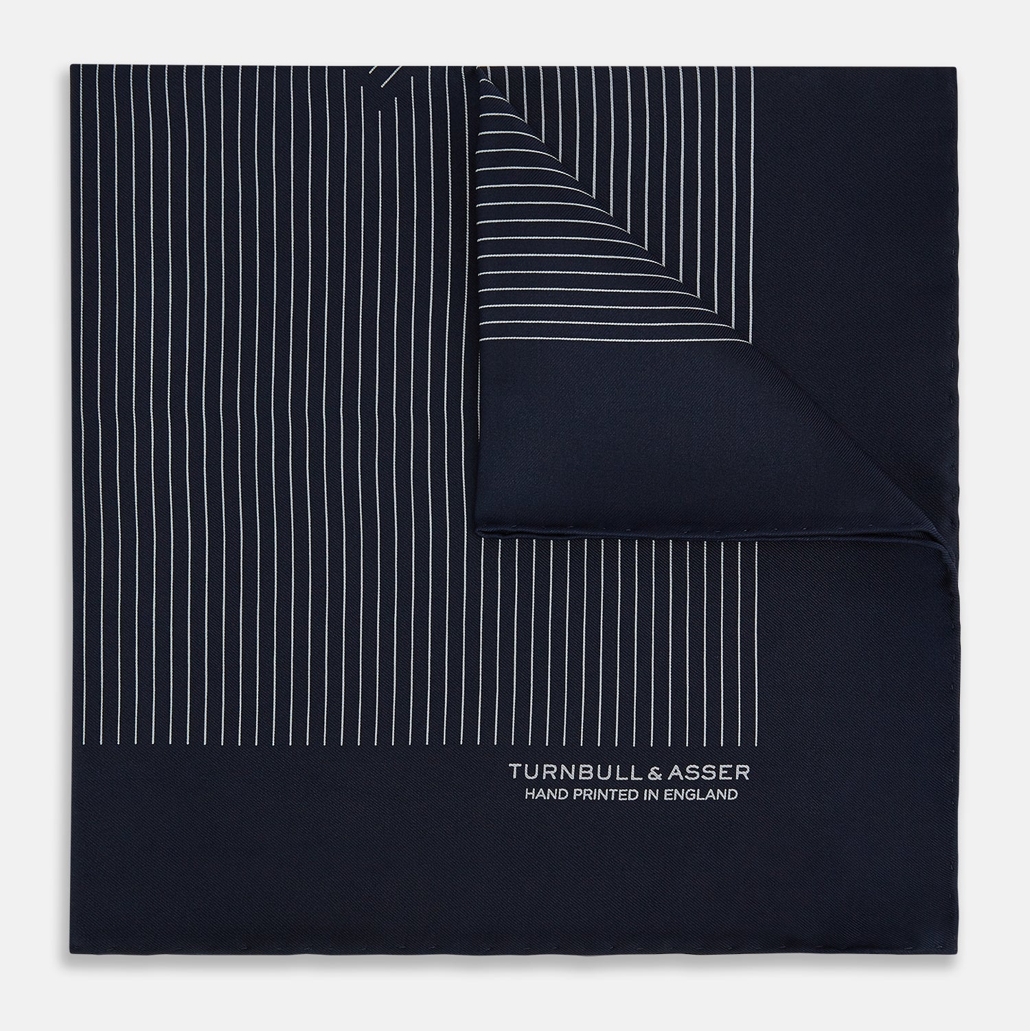 View 1 of product A Navy and Grey Stripe Silk Pocket Square by Turnbull & Asser, featuring hand-rolled edges and brand text in the corner. One corner is folded to show the reverse side.