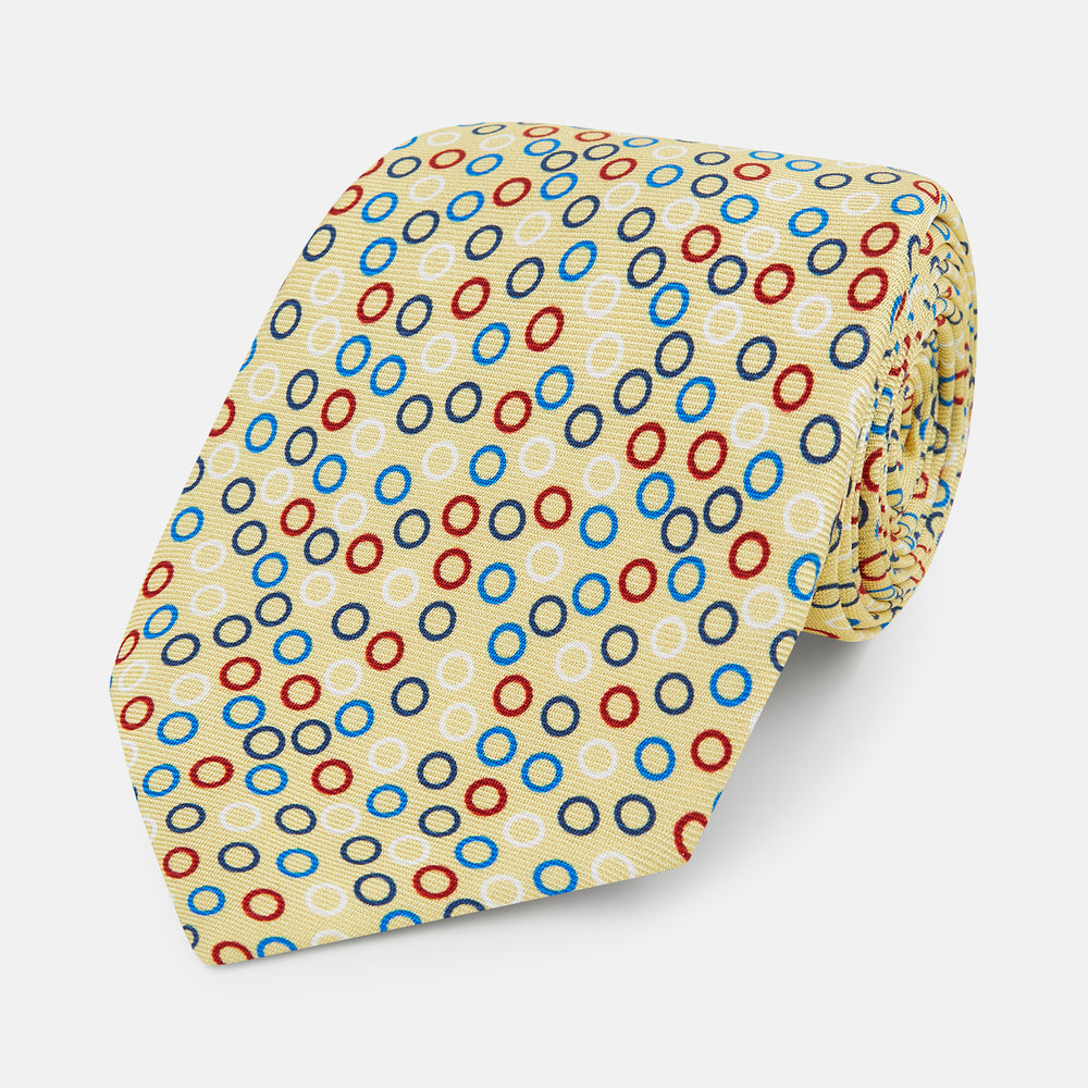 The Turnbull & Asser Multi-coloured Circle Yellow Silk Tie, crafted from fine English silk, features a vibrant pattern of multicoloured circles and is elegantly displayed rolled on a white background.