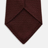View 4 of product The Turnbull & Asser Dark Red Knitted Tie, featuring a textured finish, is shown rolled up against a white background—a stylish and versatile accessory ideal for the modern gentleman.