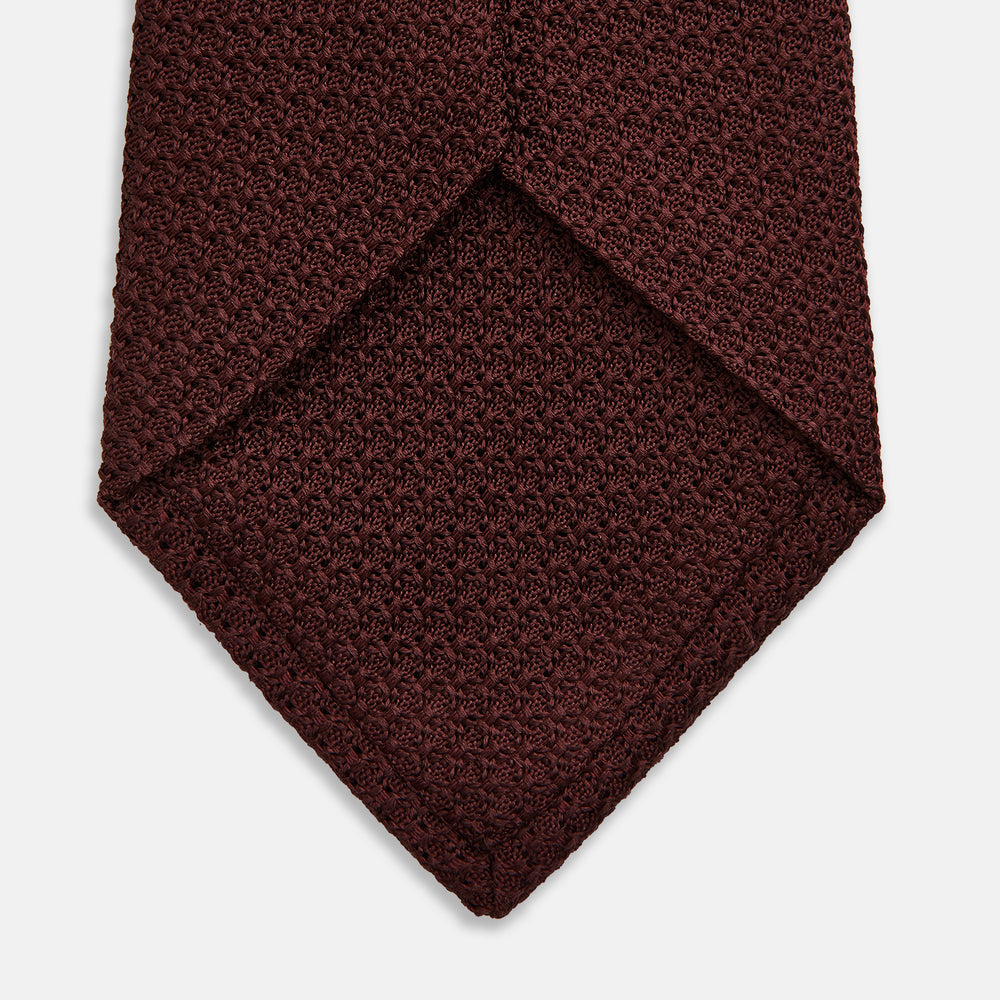 The Turnbull & Asser Dark Red Knitted Tie, featuring a textured finish, is shown rolled up against a white background—a stylish and versatile accessory ideal for the modern gentleman.