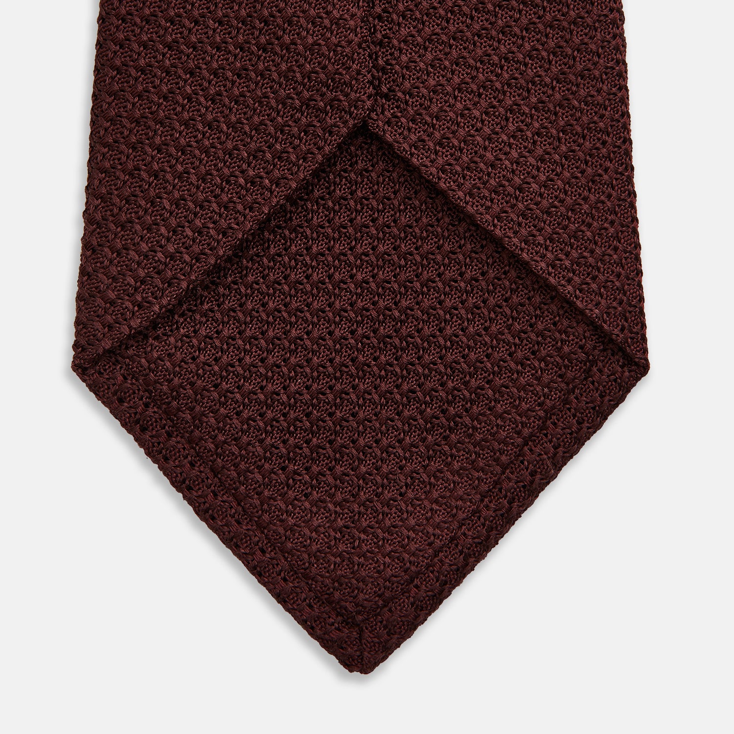 View 4 of product The Turnbull & Asser Dark Red Knitted Tie, featuring a textured finish, is shown rolled up against a white background—a stylish and versatile accessory ideal for the modern gentleman.