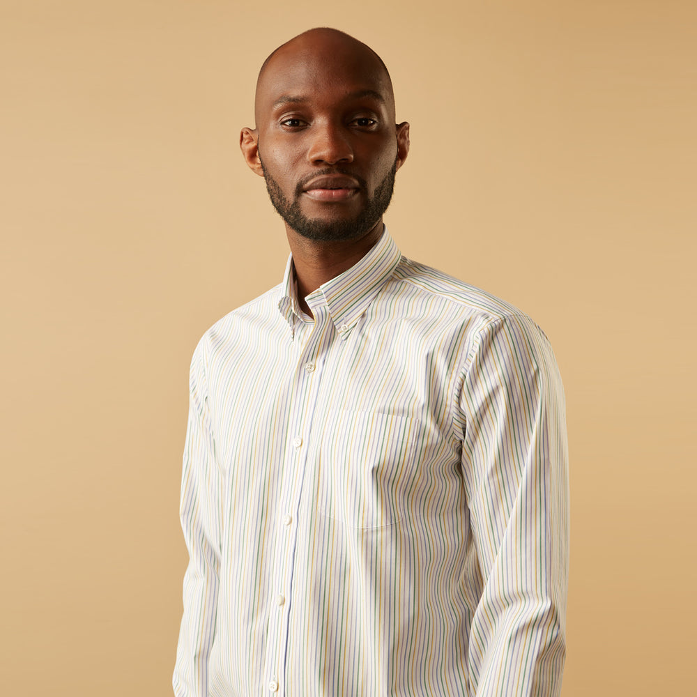 A man wears the Turnbull & Asser Yellow Multi Blazer Stripe Weekend Fit Suffolk Shirt, standing against a beige background with his hands relaxed—a casual look perfect for weekends.