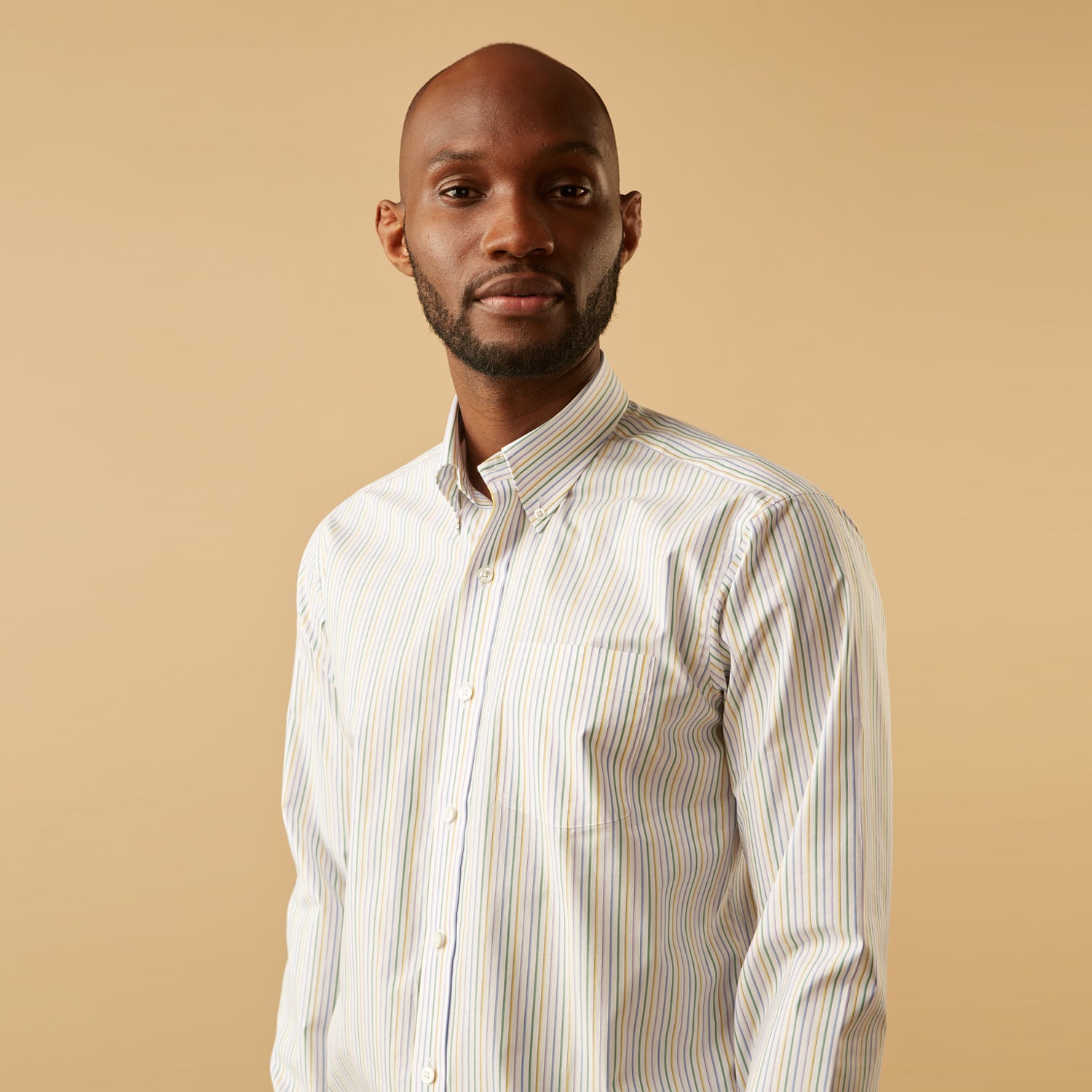 View 4 of product A man wears the Turnbull & Asser Yellow Multi Blazer Stripe Weekend Fit Suffolk Shirt, standing against a beige background with his hands relaxed—a casual look perfect for weekends.