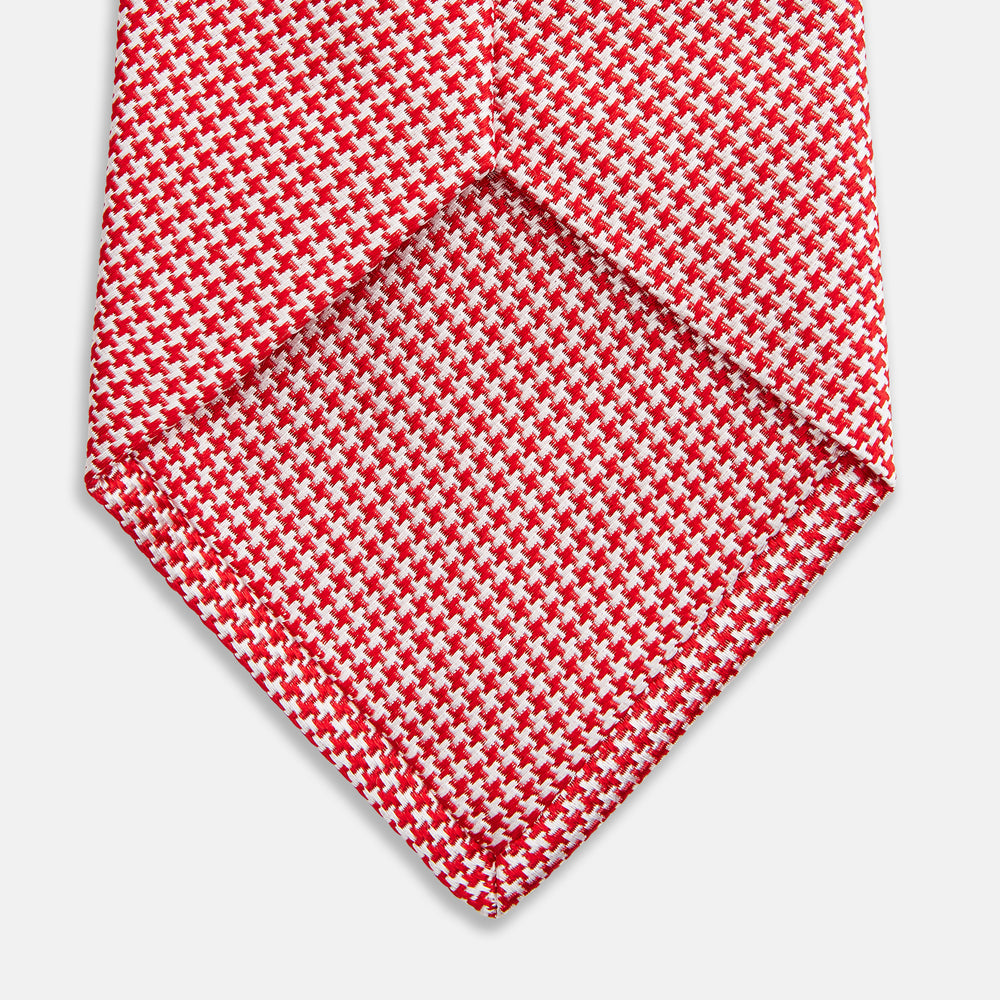 The Turnbull & Asser Red and White patterned silk tie, crafted from fine silk with a small geometric design, is elegantly rolled and displayed on a white background—a refined men’s accessory.