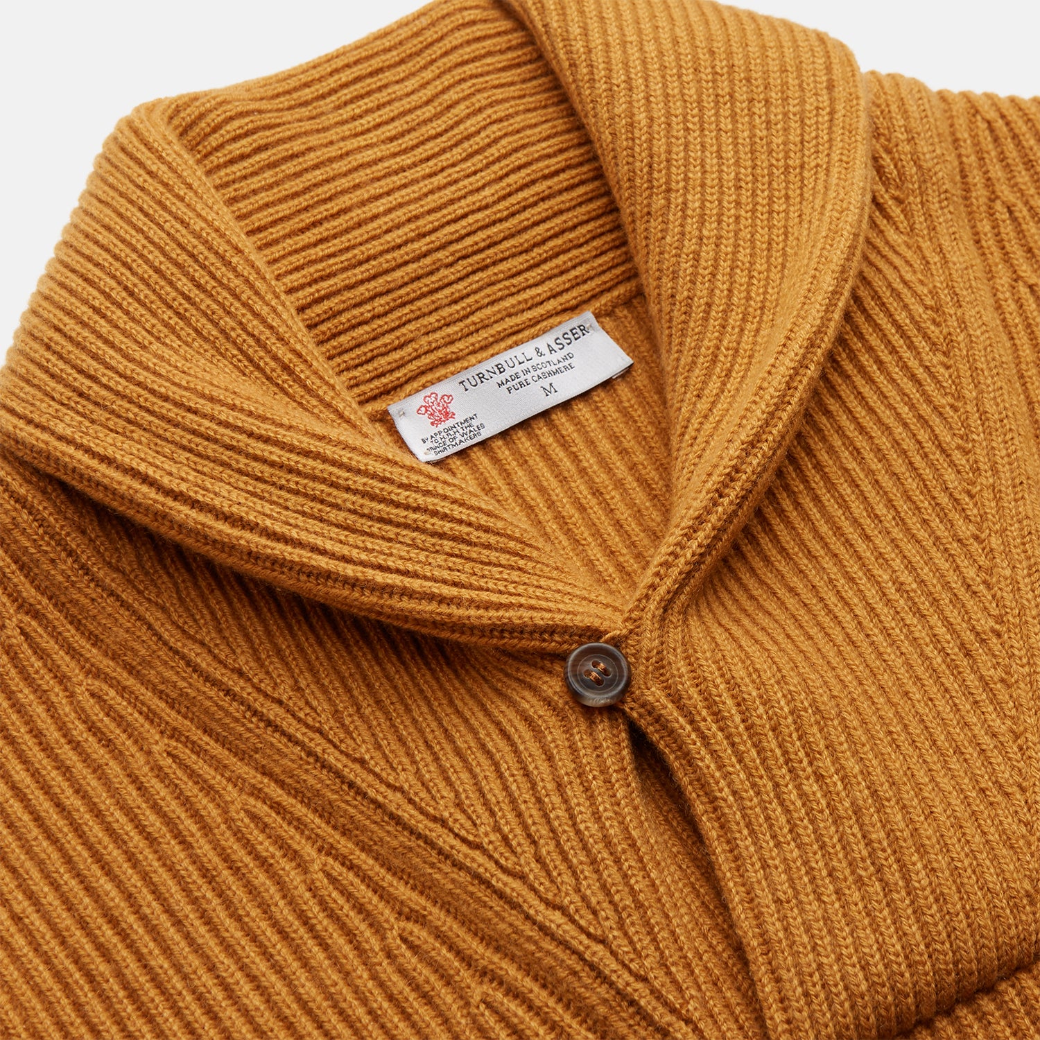 View 2 of product The Turnbull & Asser Gold Cashmere Shawl Neck Lytton Jumper, in ribbed knit with a horn button at the neckline, is stylishly laid flat on a white background.