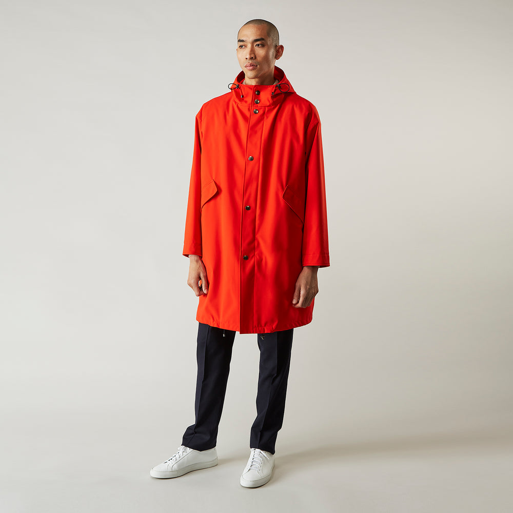Wearing the Turnbull & Asser Red Walter Sealup Parka with Detachable Liner, black pants, and white sneakers, a person stands in profile against a plain light background—perfect for travel.