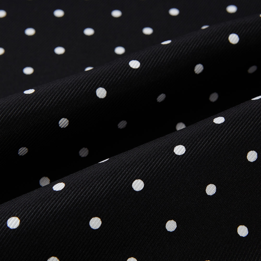 The Turnbull & Asser Black and White Spotted Silk Scarf with Fringes features a classic polka dot design, silver fringe edges, and the brand name printed near each end.