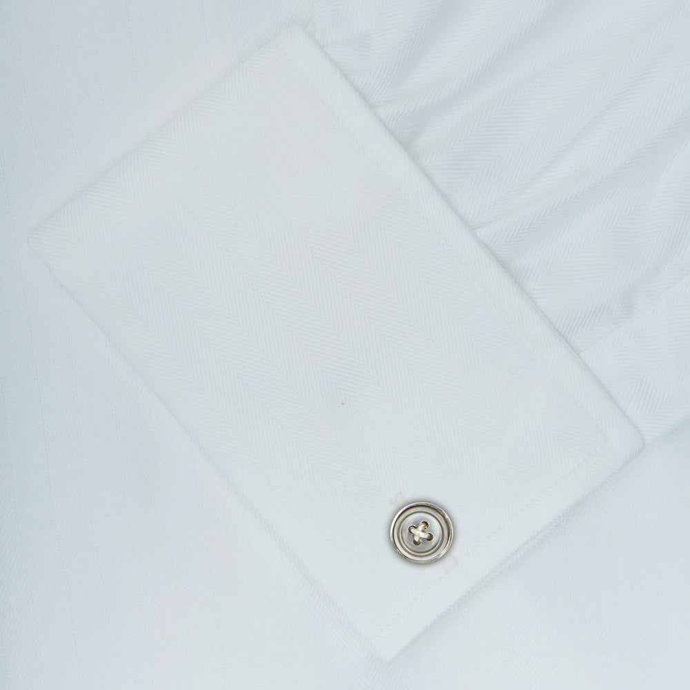 The Turnbull & Asser White Herringbone Superfine Cotton Shirt features a T&A collar, double cuffs, and a visible label inside the collar, shown neatly folded on a light blue background—ideal for minimalist looks or pairing with bold ties.
