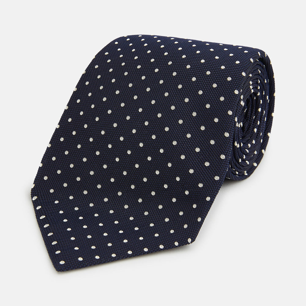 The Silver and Navy Micro Dot Silk Tie by Turnbull & Asser features a refined micro dot pattern, perfect for adding a classic accent to formal attire. Shown neatly rolled on a white background.