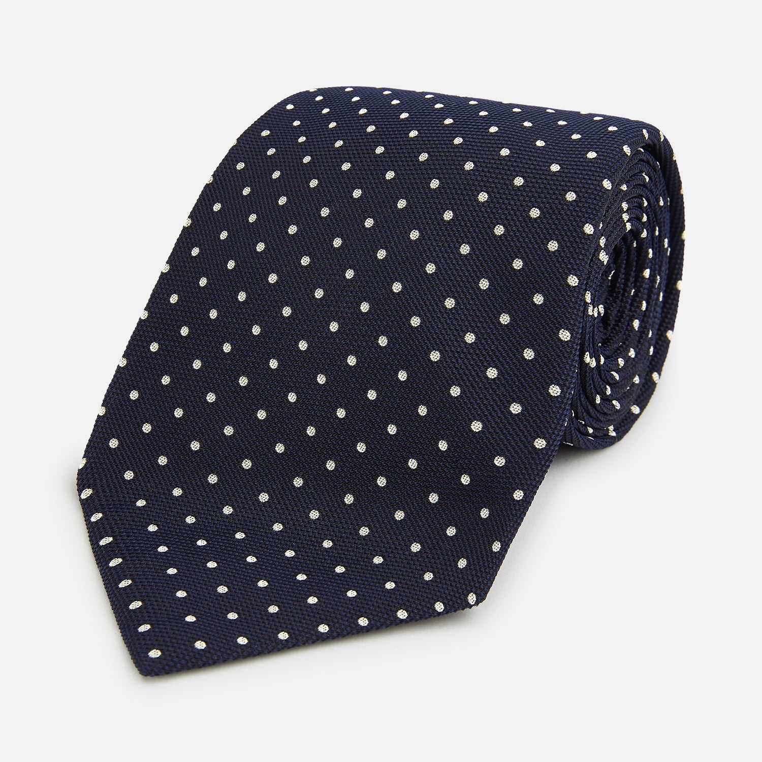 View 1 of product The Silver and Navy Micro Dot Silk Tie by Turnbull & Asser features a refined micro dot pattern, perfect for adding a classic accent to formal attire. Shown neatly rolled on a white background.