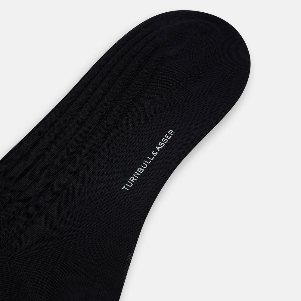 A single Midnight Mid-length Sock by Turnbull & Asser, made from mercerised Egyptian cotton, stands upright on a white background. This luxury black sock features a ribbed texture with smooth toe and heel areas.