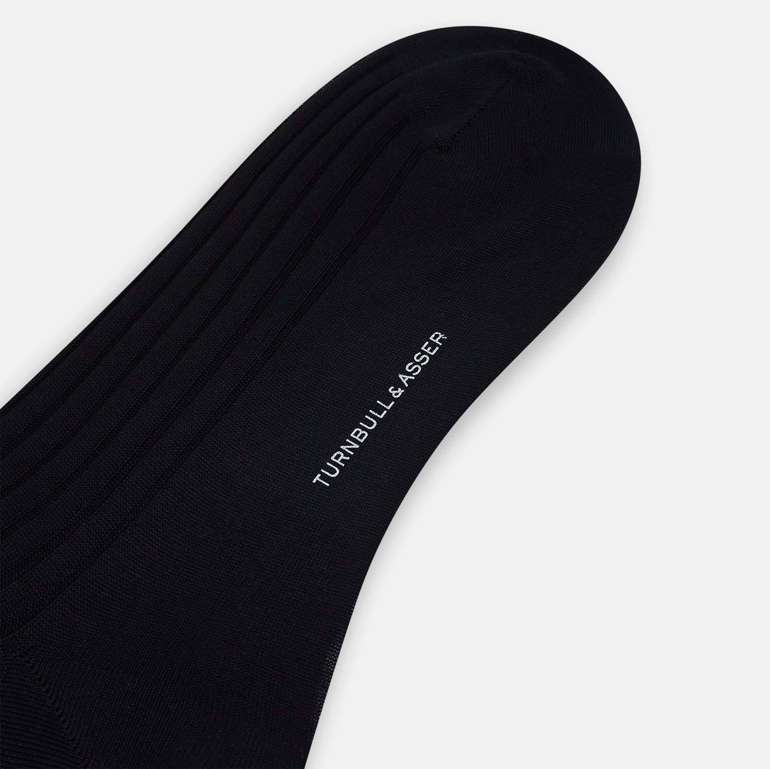 View 3 of product A single Midnight Mid-length Sock by Turnbull & Asser, made from mercerised Egyptian cotton, stands upright on a white background. This luxury black sock features a ribbed texture with smooth toe and heel areas.