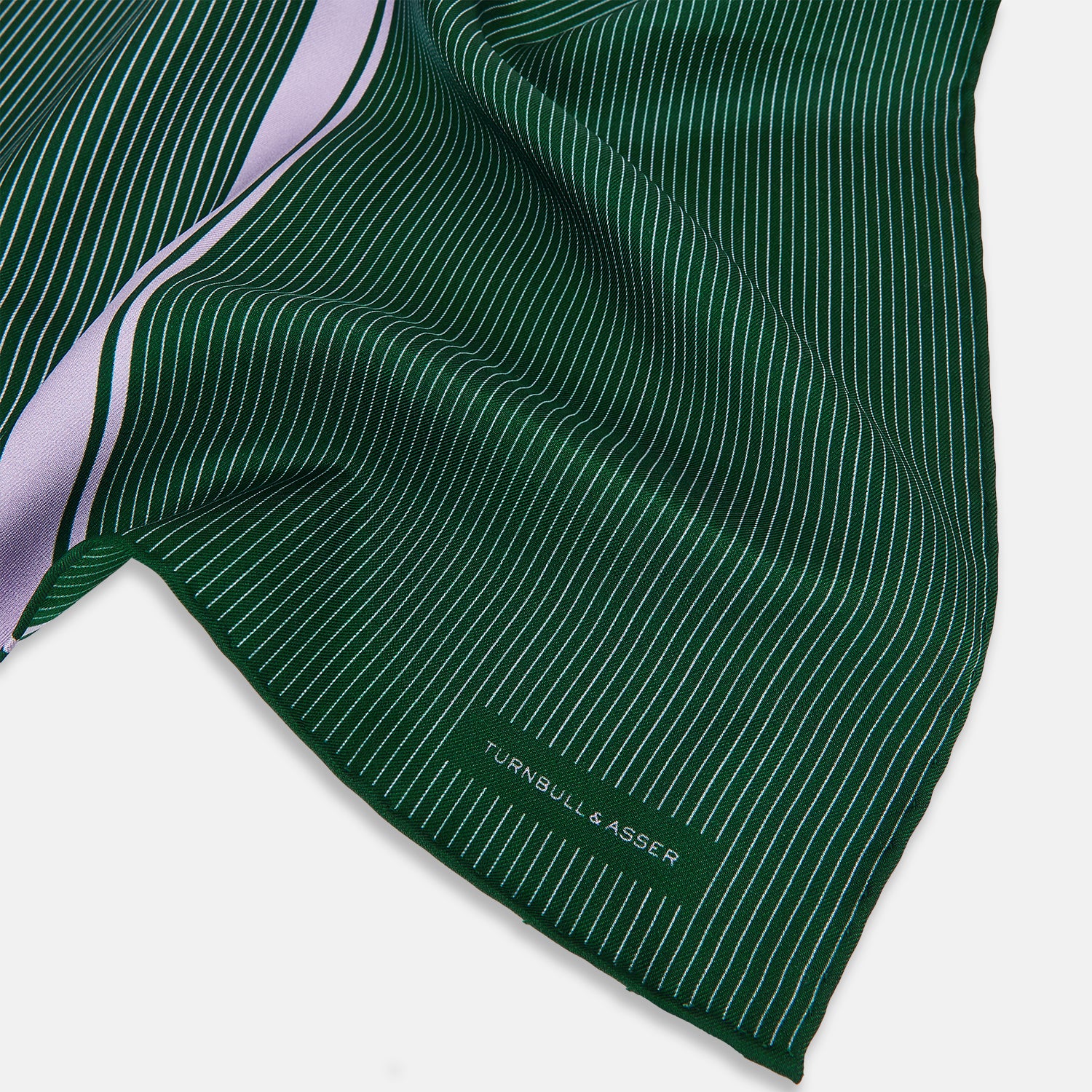 View 2 of product The Forest Green and Lilac Stripe Silk Pocket Square by Turnbull & Asser features thin white pinstripes, a bold light purple vertical stripe, and a visible branded label for classic British elegance. One corner is neatly folded over.