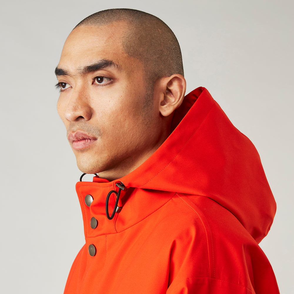 Wearing the Turnbull & Asser Red Walter Sealup Parka with Detachable Liner, black pants, and white sneakers, a person stands in profile against a plain light background—perfect for travel.