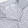 View 6 of product A man wearing glasses and a Pale Blue Multi Check Cashmerello Holiday Fit Winnington Shirt by Turnbull & Asser leans casually against a white countertop, looking at the camera with a neutral expression.