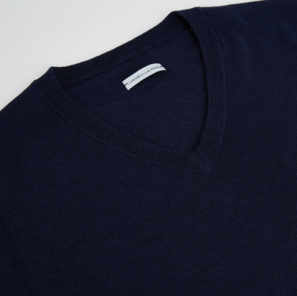 The Turnbull & Asser Navy Fine Merino V-Neck Jumper is displayed against a white background, featuring ribbed cuffs and hem for timeless style in a classic, plain long-sleeve design.