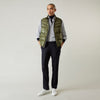 View 1 of product A man stands against a plain background wearing the Turnbull & Asser Green Peyton Sealup Quilted Gilet over a striped shirt, dark trousers, and white sneakers, with his hands in his pockets and looking slightly to the side.