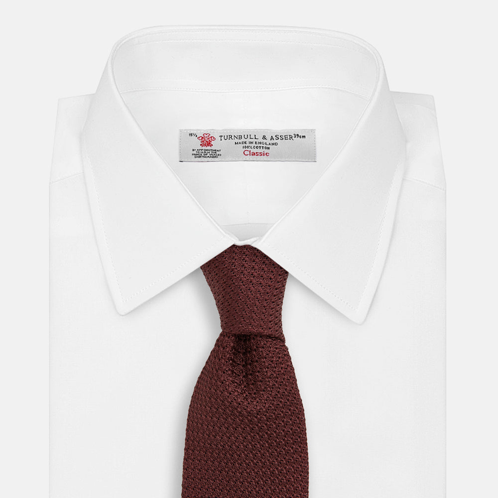 The Turnbull & Asser Ruby Red Knitted Tie, shown rolled-up against a white background, is a textured silk accessory that adds versatile sophistication to any gentleman's wardrobe.