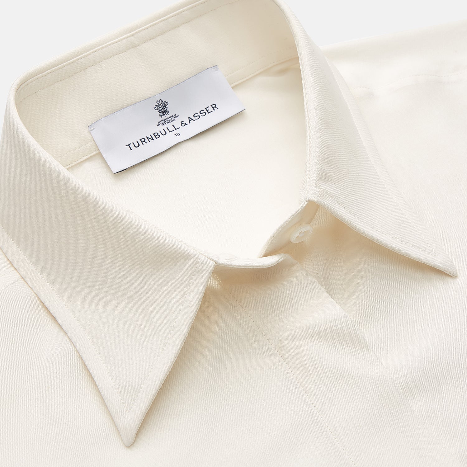 View 2 of product The Cream Silk Tailored Bianca Shirt by Turnbull & Asser features long sleeves, a pointed collar, and curved hem in soft-touch peace silk with a tailored fit. Shown laid flat on a white background.