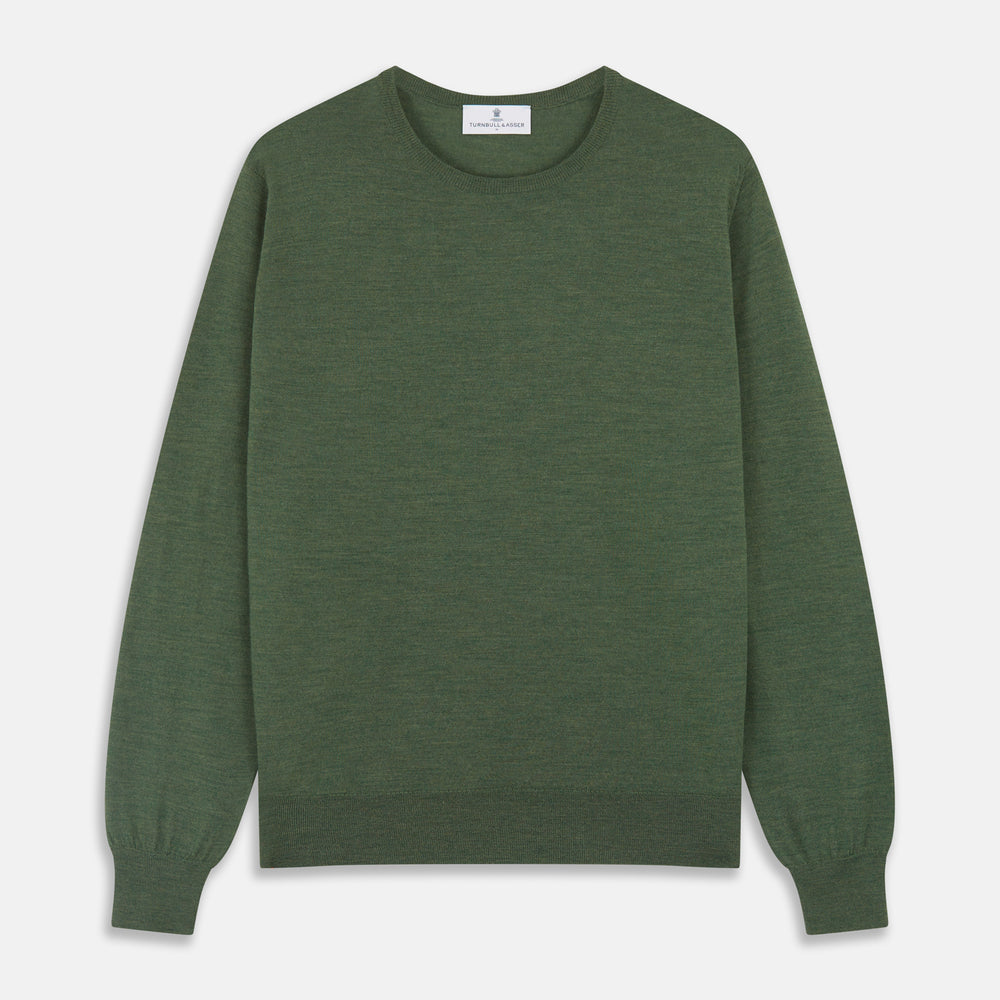 A man stands facing the camera against a plain light background, wearing the Turnbull & Asser Bottle Green Merino Kingston Crew Neck Jumper with dark pants and black shoes. His arms rest at his sides and he has a neutral expression.