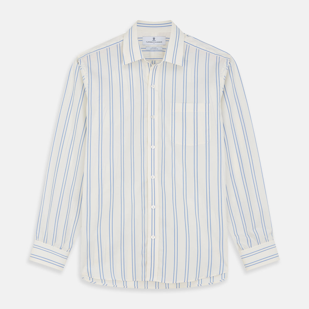 A man with short brown hair stands against a beige background in a Turnbull & Asser Blue and Off-White Stripe Cotton Weekend Fit Finch Shirt, featuring vertical stripes and a Derby collar, paired with dark pants. One hand is in his pocket; he has a neutral expression.