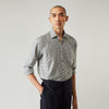View 1 of product A person with a shaved head models the Turnbull & Asser Grey Check Weekend Fit Flannel Shirt with a Derby collar and 1-button cuffs, sleeves rolled up, paired with dark trousers against a plain background, gazing directly at the camera.