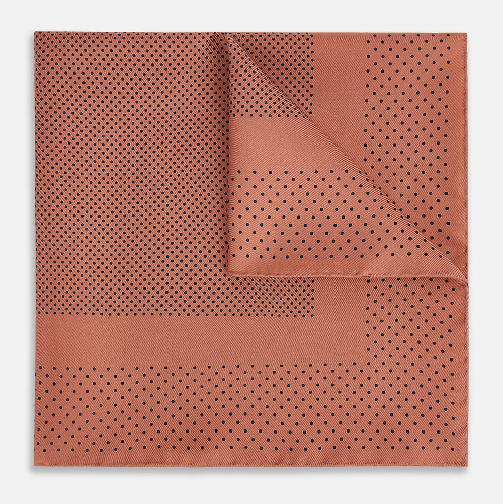 The Turnbull & Asser Blush Dot Silk Pocket Square features a rust hue with black polka dots, a bordered design, and hand-rolled edges, shown folded against a white background.