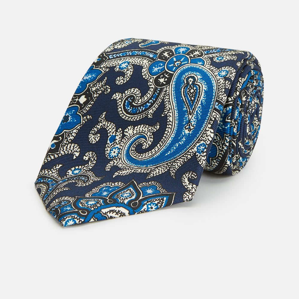 The Turnbull & Asser Blue and Navy Twisted Paisley Silk Tie displays intricate blue, white, and black details, rolled up against a plain white background.
