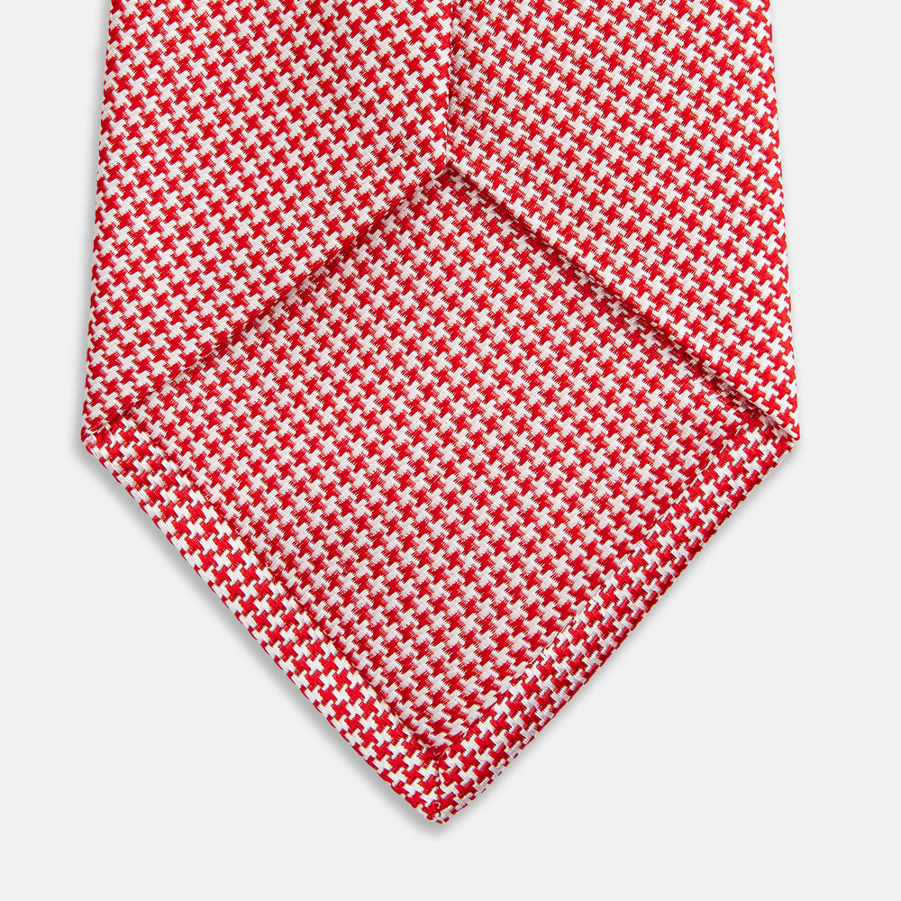 The Turnbull & Asser Red Houndstooth Silk Tie features a textured, small geometric pattern in red and white—ideal as a classic office accessory, shown rolled up on a plain white background.