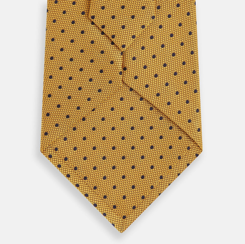 The Turnbull & Asser Navy and Yellow Micro Dot Silk Tie features evenly spaced dark blue micro dots on yellow silk, rolled and displayed on a white background—an elegant accessory for any occasion.