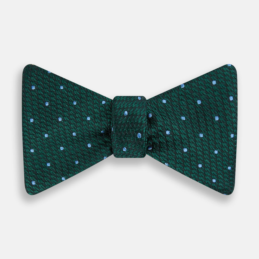 The Turnbull & Asser Forest Green and Sky Blue Spot Houndstooth Silk Bow Tie features a textured pattern with light blue polka dots, shown against a plain white background.