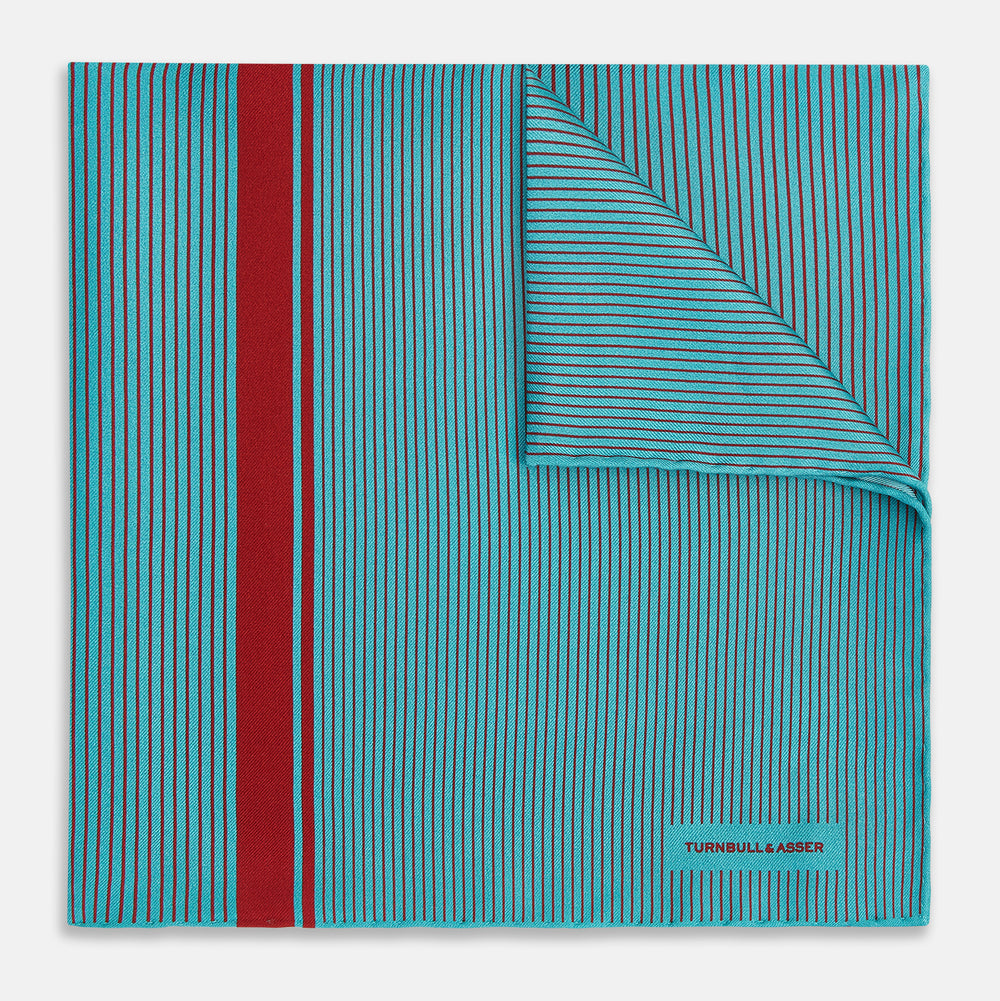 The Turnbull & Asser Turquoise and Red Stripe Silk Pocket Square features thin navy stripes with a bold vertical red stripe, partially folded to reveal the reverse pattern and the brand's logo, showcasing its British heritage.