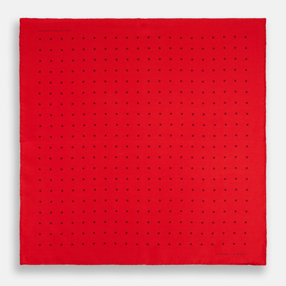 The Turnbull & Asser Red and Burgundy Spot Silk Pocket Square features evenly spaced small spots and the brand logo in the bottom right corner—perfect for formal wear. One corner is folded to show the reverse side.