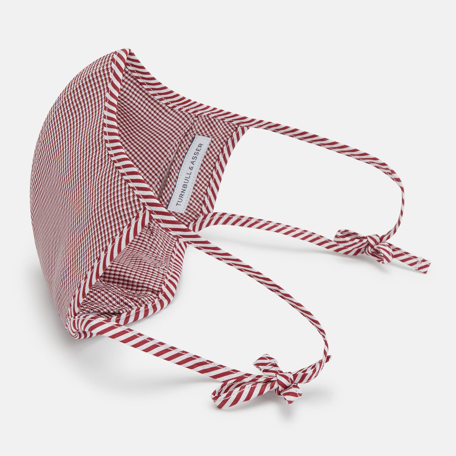View 4 of product The Turnbull & Asser Burgundy Check Commuter Mask comes with 3 Viroformula™ filters. It features a check pattern, adjustable ear straps, and is displayed on a plain white background.