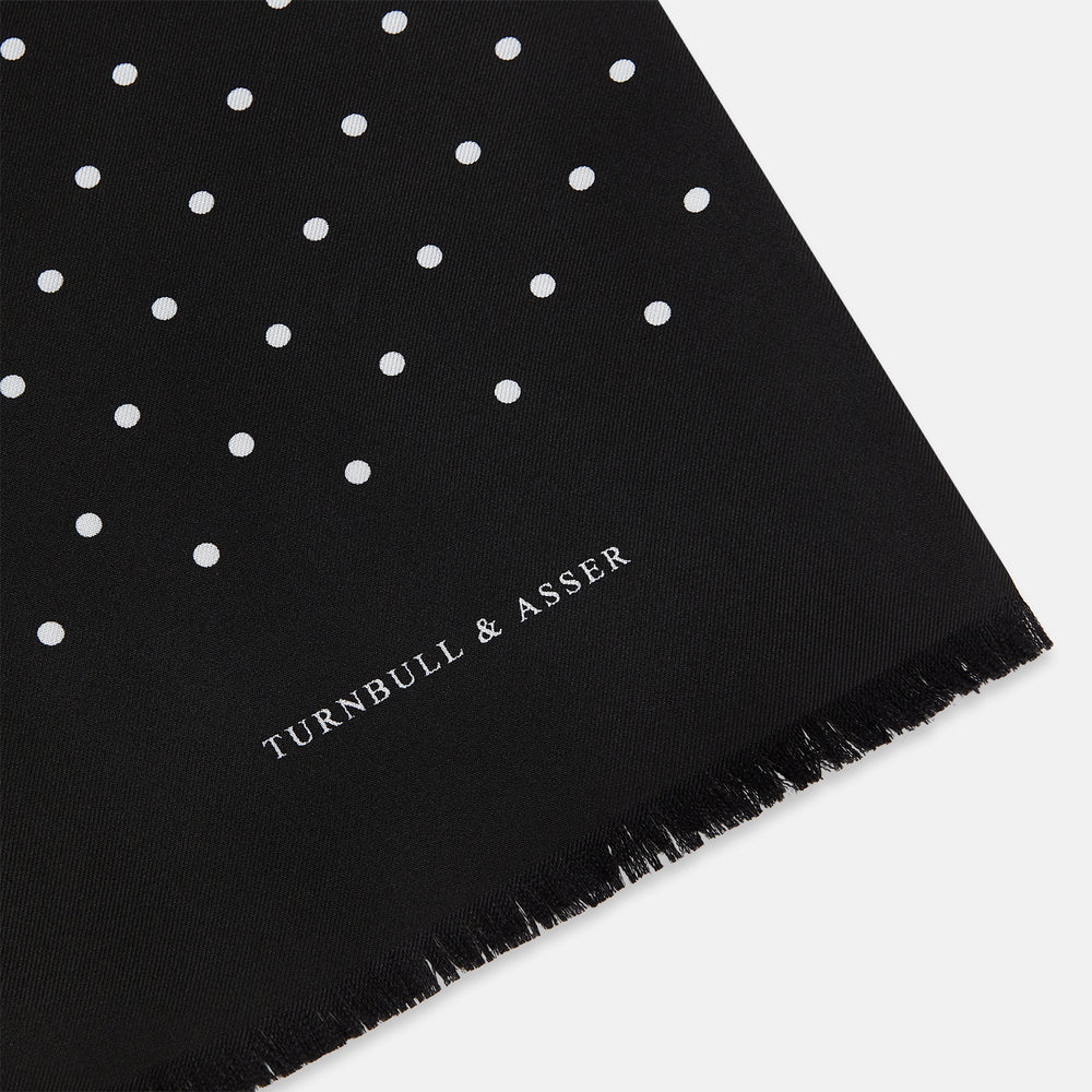 The Black and White Spotted Silk Scarf by Turnbull & Asser features a spotted design, neatly folded at the top and spread out at the bottom, with the brand's name printed in white near its fringed ends.