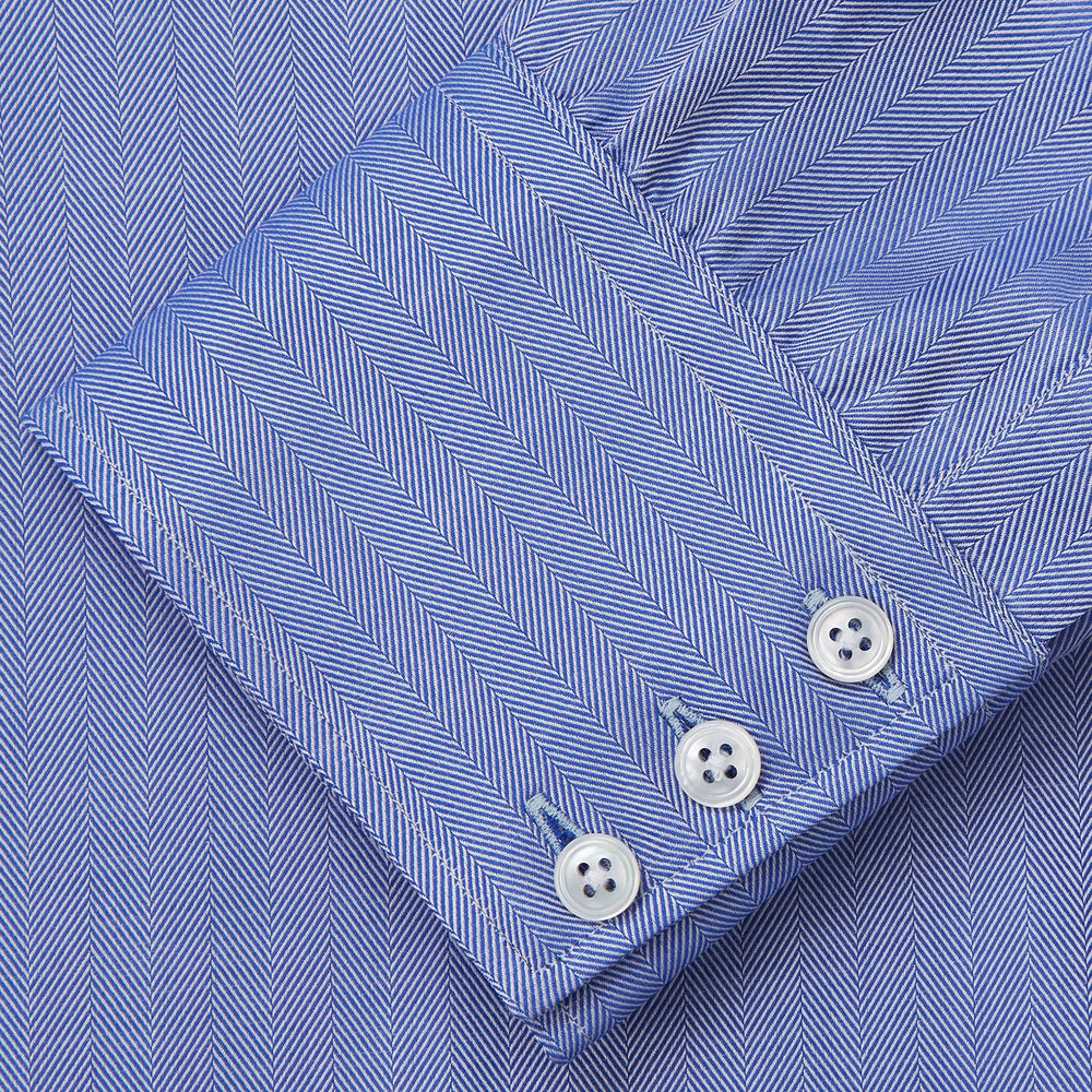 Turnbull & Asser's Blue Herringbone Tailored Fit Shirt with a Kent collar and white buttons is shown laid flat on a white background.