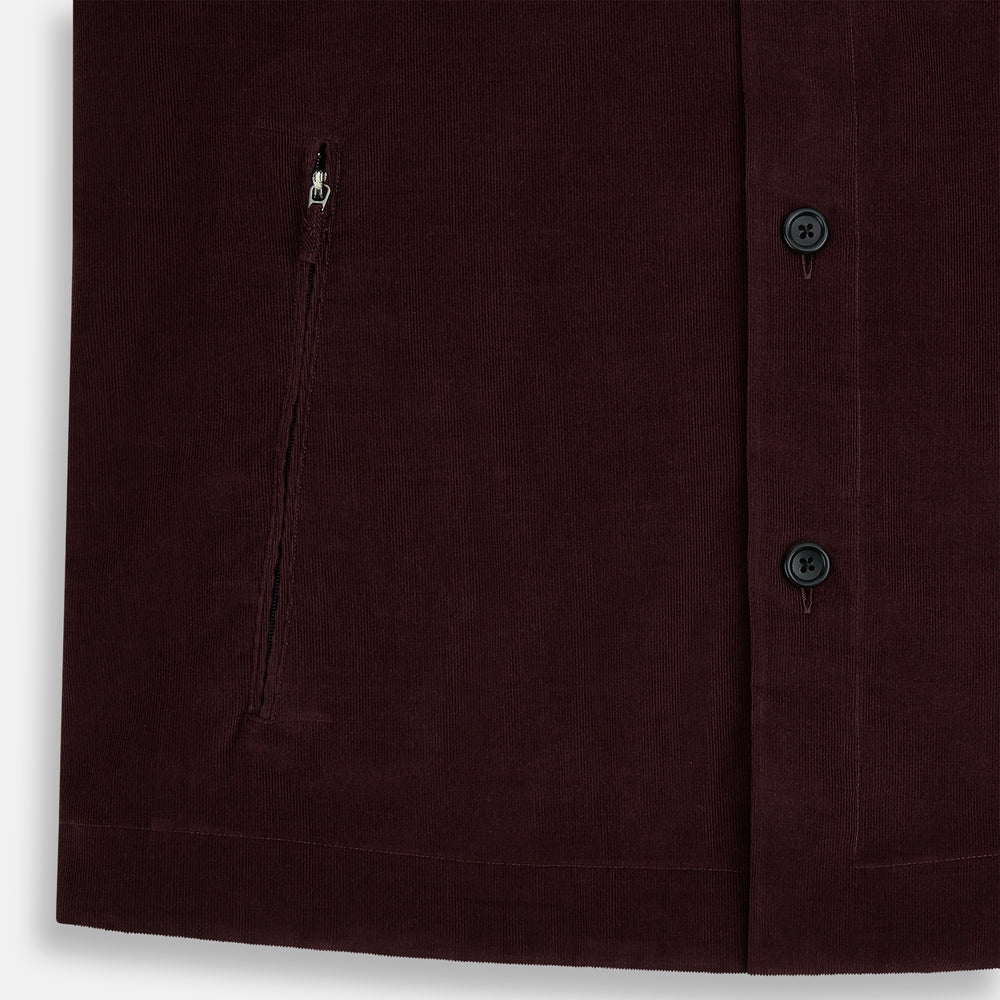 The Turnbull & Asser Burgundy Corduroy Hampstead Overshirt features long sleeves, a collar, a large left chest pocket, and two zippered side pockets, shown laid flat on a plain white background.