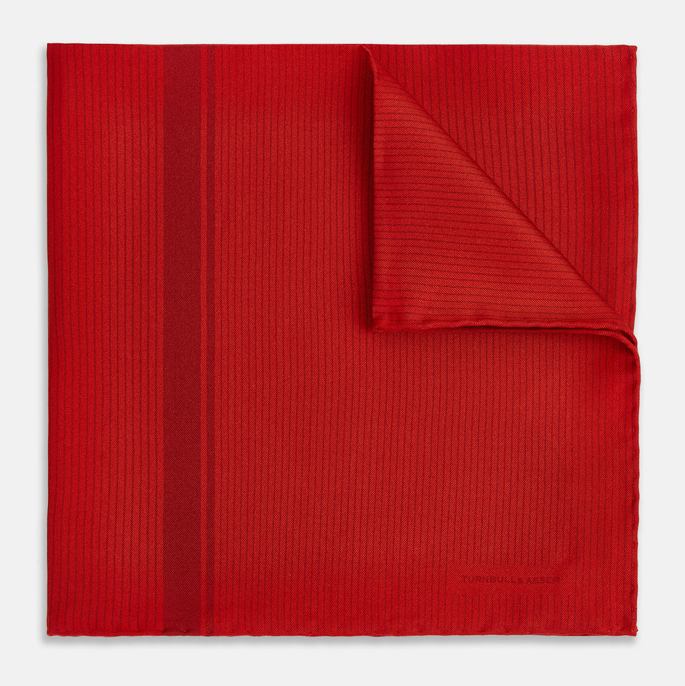The Red and Burgundy Stripe Silk Pocket Square by Turnbull & Asser features subtle vertical stripes and a darker red stripe along one side, with “Turnbull & Asser” embossed in the fabric and a textured, turned-down corner.
