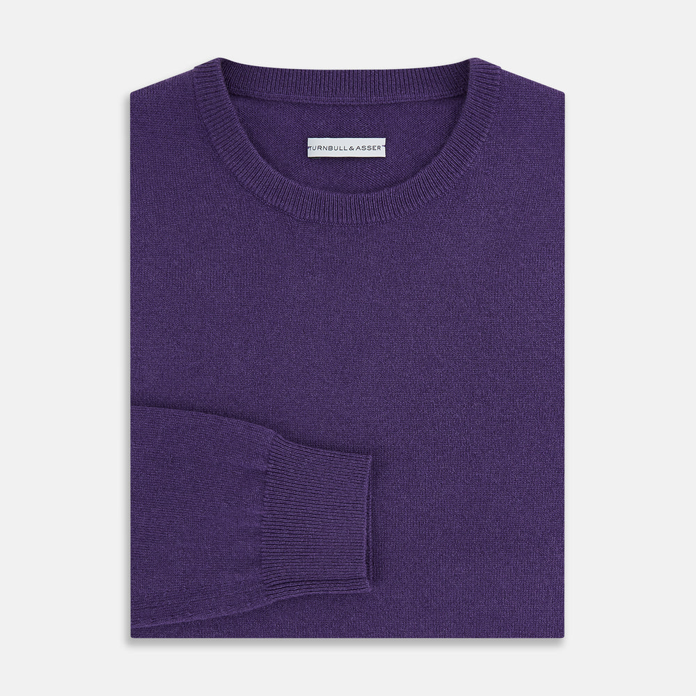 The Turnbull & Asser Purple Cashmere Round Neck Jumper features long sleeves, ribbed cuffs, hem, and collar for an elegant silhouette. This versatile knitwear piece is shown against a white background.