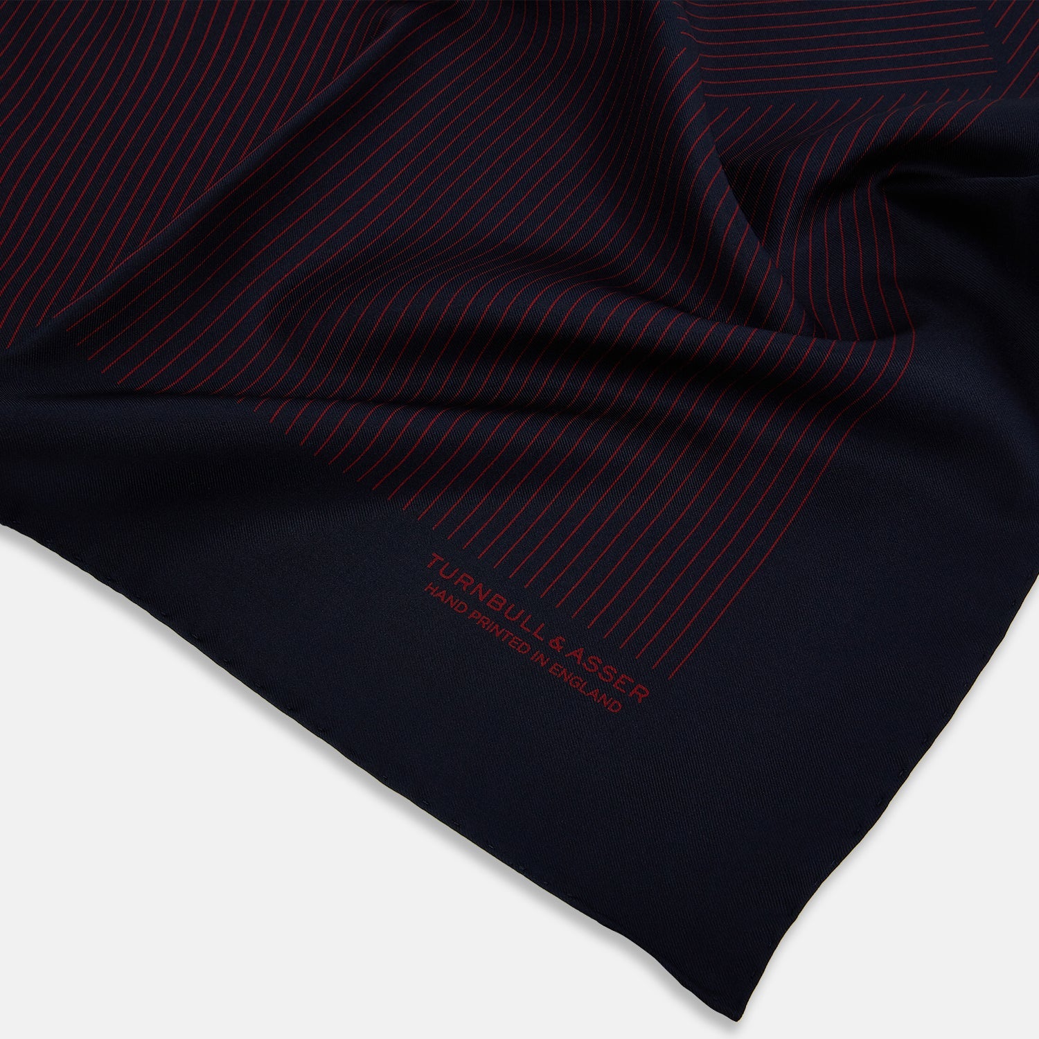 View 2 of product The Turnbull & Asser Navy and Burgundy Stripe Silk Pocket Square features diagonal stripes in one corner, hand-rolled edges, and "TURNBULL & ASSER HAND PRINTED IN ENGLAND" printed in red on luxurious silk.