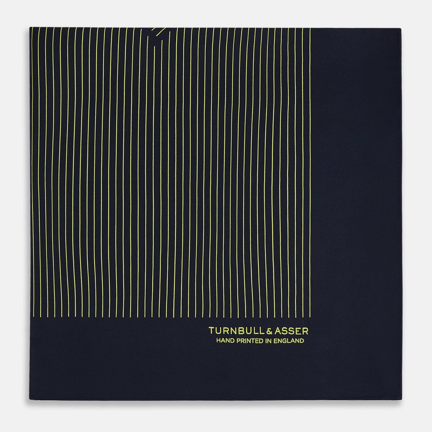 View 4 of product The Turnbull & Asser Navy and Gold Stripe Silk Pocket Square features light yellow vertical stripes, a folded corner, and "TURNBULL & ASSER HAND PRINTED IN ENGLAND" in gold at the bottom right.