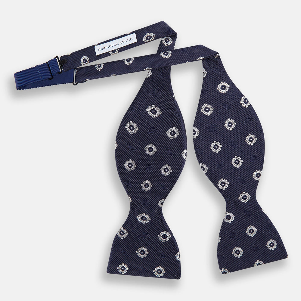 The Navy and White Motif Silk Bow Tie by Turnbull & Asser features a geometric floral pattern, adding refined elegance to formalwear. Shown on a plain white background.