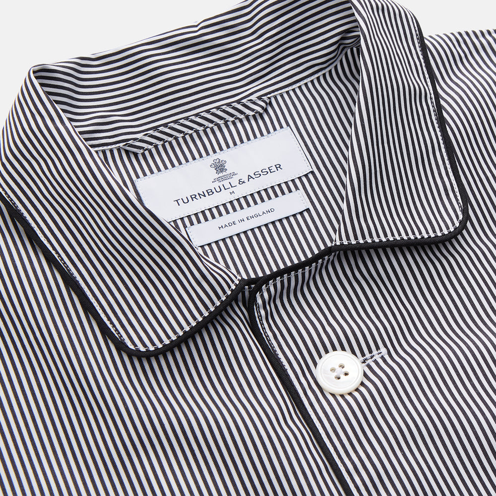 The Turnbull & Asser Black Candy Stripe Cotton Hyde Pyjama Set for men features soft cotton striped pajamas with a long-sleeve, button-up shirt detailed with black piping and three pockets, plus matching pants, both laid flat on a white background.