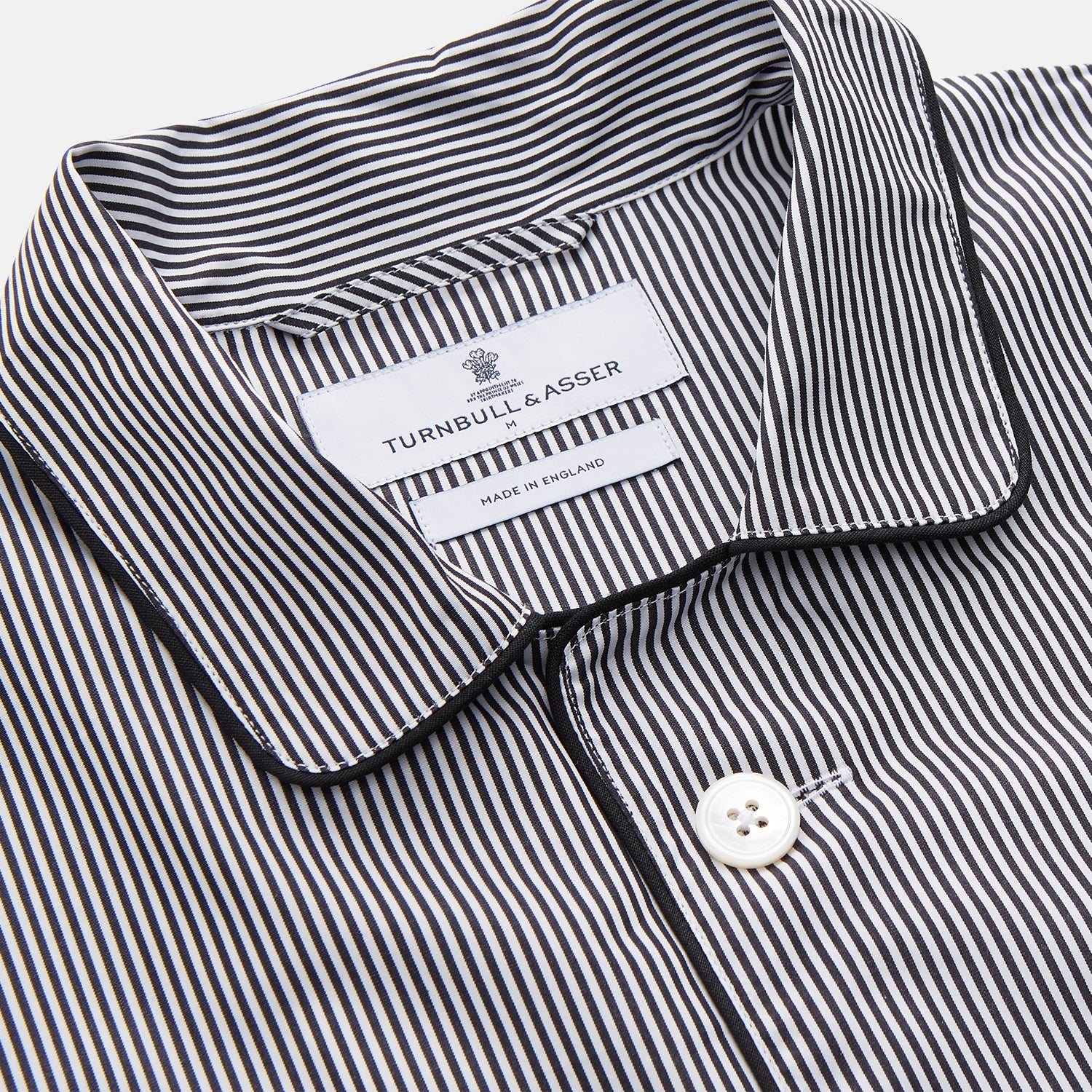 View 5 of product The Turnbull & Asser Black Candy Stripe Cotton Hyde Pyjama Set for men features soft cotton striped pajamas with a long-sleeve, button-up shirt detailed with black piping and three pockets, plus matching pants, both laid flat on a white background.
