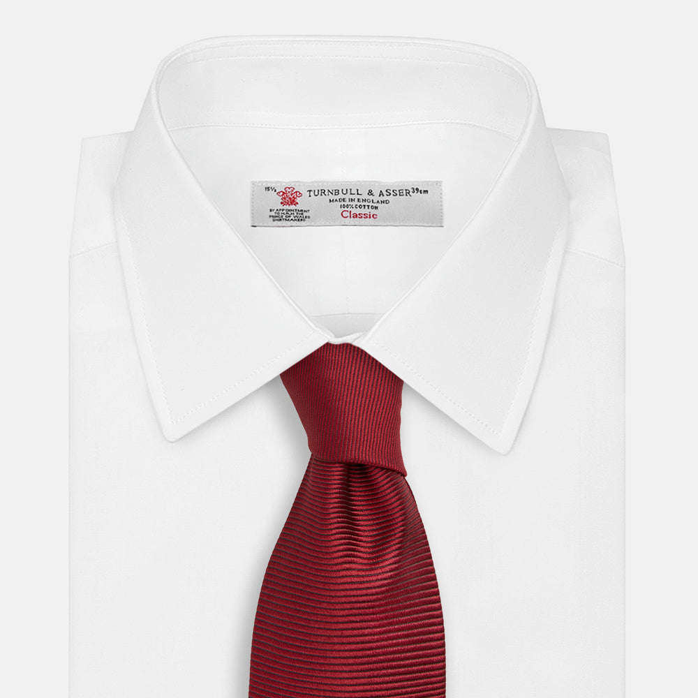 A close-up of the Turnbull & Asser HORIZONTAL TWILL BURGUNDY TIE, a textured men's accessory, rolled up and displayed on a plain white background.