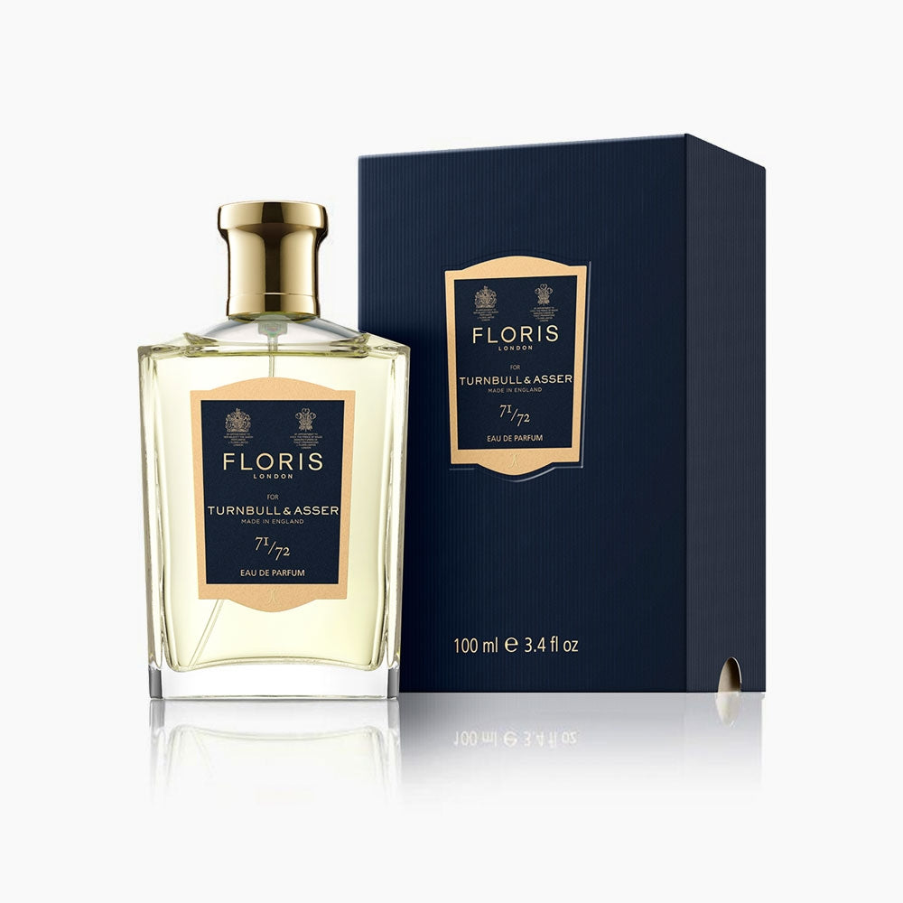 A bottle of Floris 71/72 Eau De Parfum by Turnbull & Asser, a woody aromatic scent, stands beside its navy blue and gold box. The 100 ml bottle features a gold cap in this exclusive collaboration.