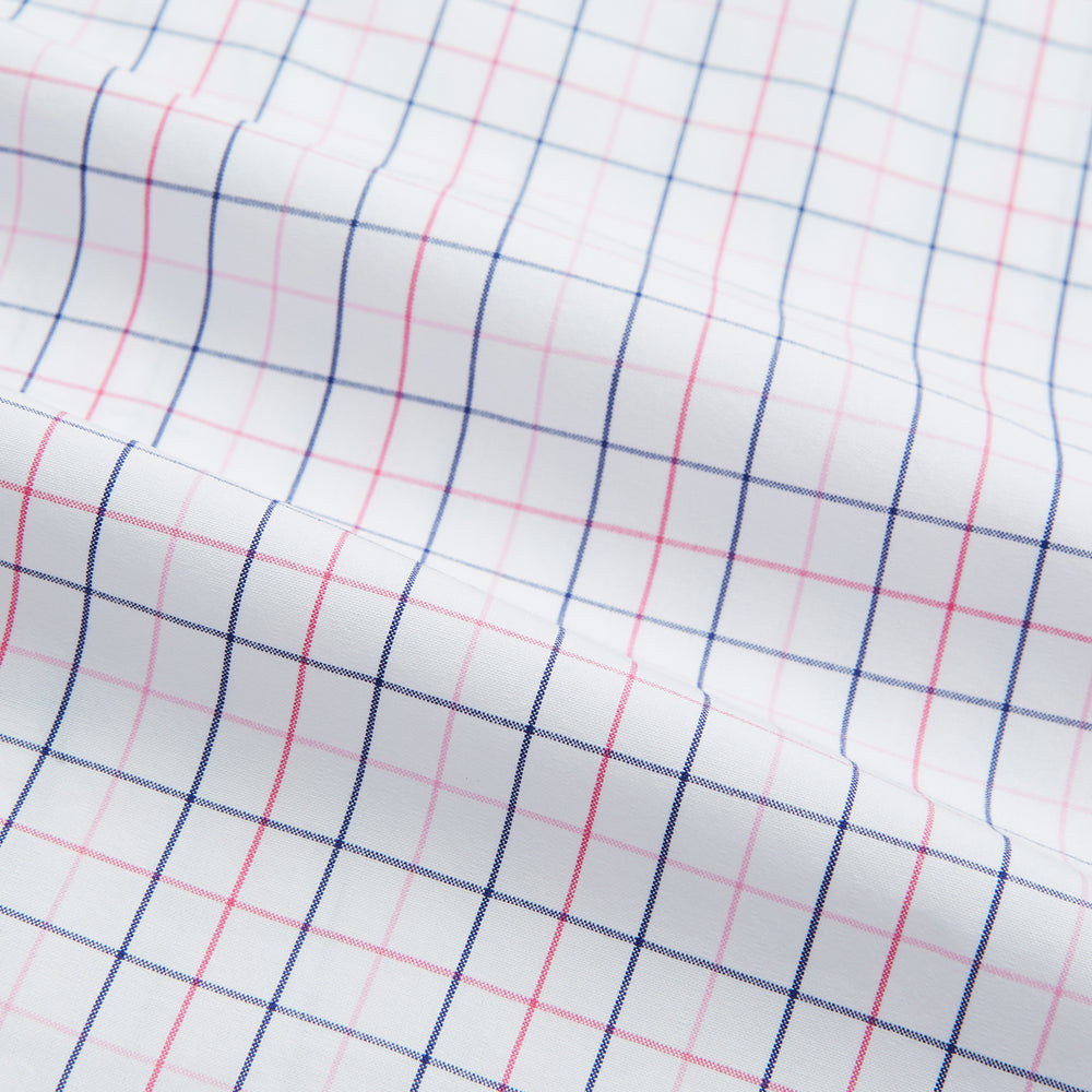 The Turnbull & Asser Pink Overlay Grid Check Mayfair Shirt is a long-sleeved, button-up with a collar and buttoned cuffs, featuring a white base and thin pink grid lines. Laid flat against a white surface.